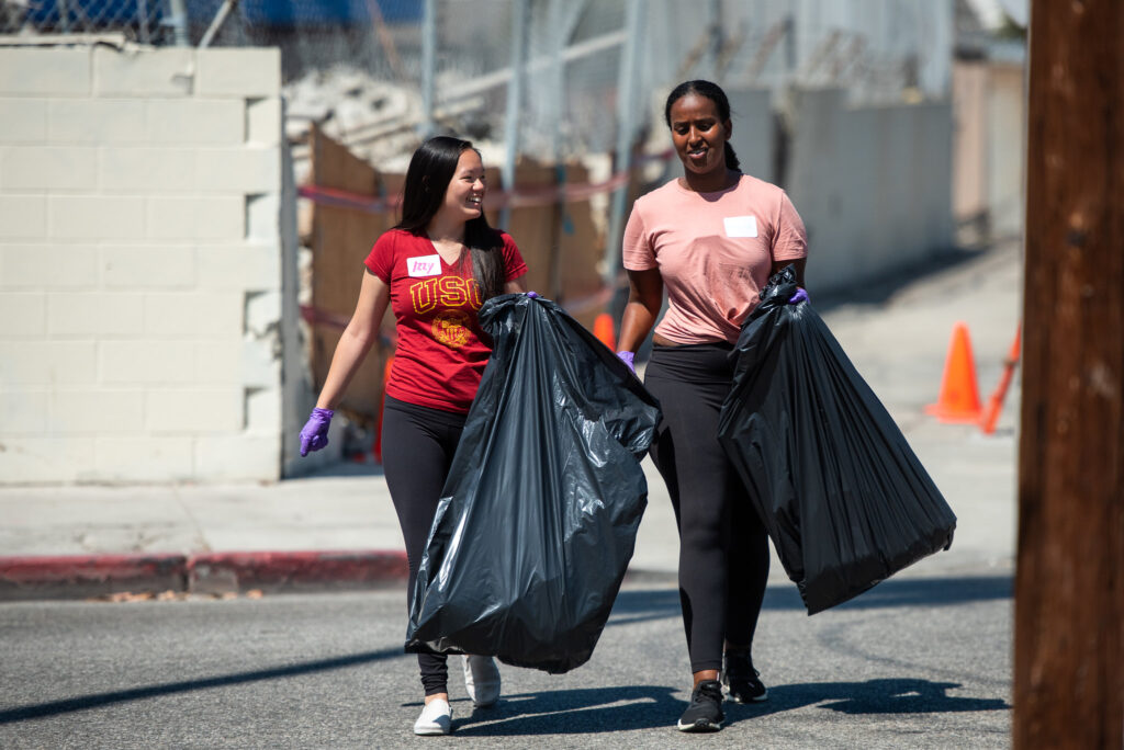 two students carrying large garbage bags