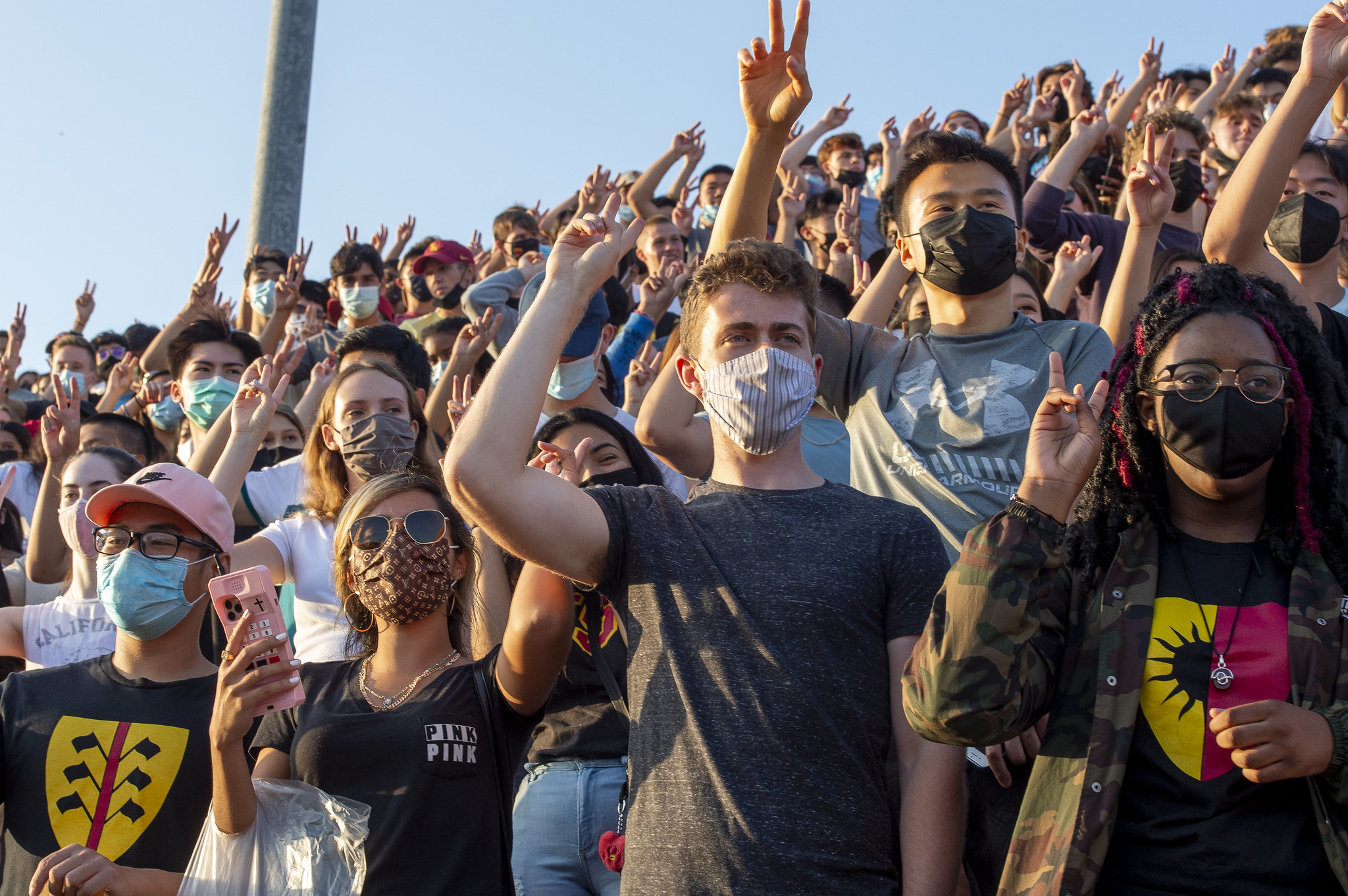 Masked students in stadium throwing USC victory symbol