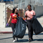two students carrying large garbage bags