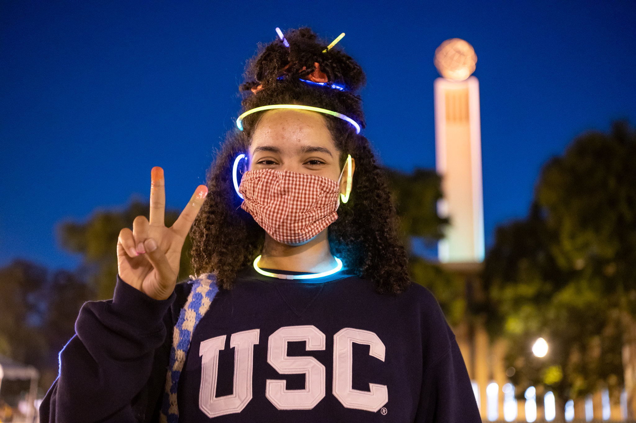 Masked student with glow sticks in hair giving fight on sign