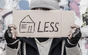 homeless person holding card board sign reading "less"